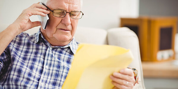 Senior man talking on mobile phone while looking at document senior scams