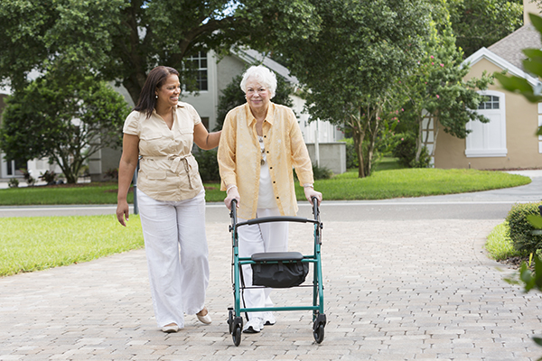 caregiver assisting senior woman with walker outside