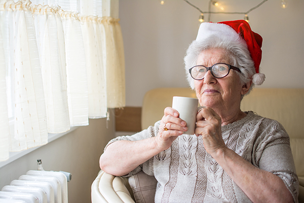 Senior woman with red Santa’s hat holding hot tea and looking through window. Xmas, home, age, alone, senior concept. Senior woman wearing santa hat