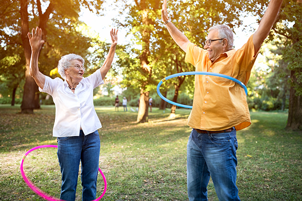 Happy and funny senior couple playing hulahop in park