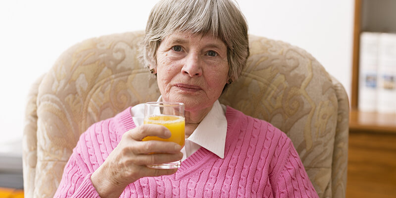 senior woman drinking orange juice in a seat at home