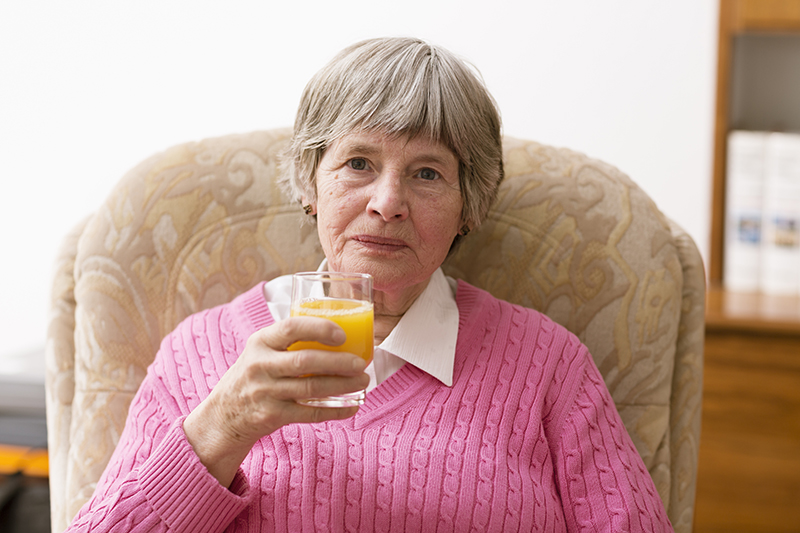 senior woman drinking orange juice in a seat at home