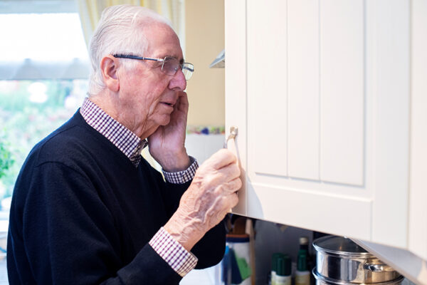 Forgetful Senior Man With Dementia Looking In Cupboard At Home Forgetful Senior Man With Dementia Looking In Cupboard At Home