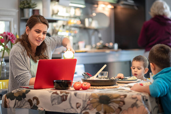 family caregiving while working on laptop at the dining table and sons having lunch