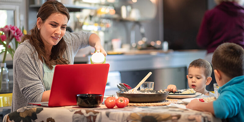 Mother working on laptop at the dining table, sons having lunch family caregiving while working on laptop at the dining table and sons having lunch