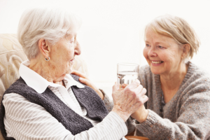 mature caregiver giving glass of water to senior woman