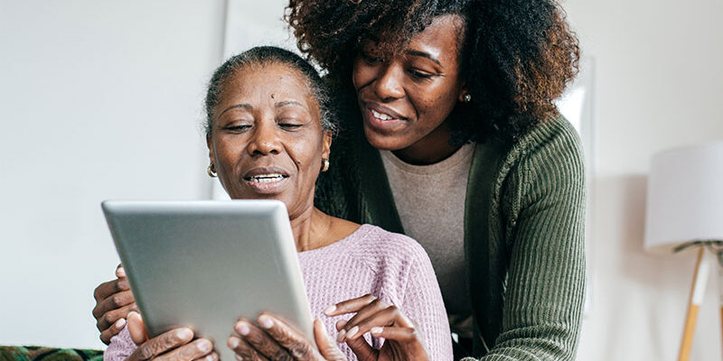 caregiver-showing-senior-lady-something-on-tablet senior lady and adult daughter looking at tablet