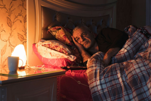 A senior man lies awake in bed at night.